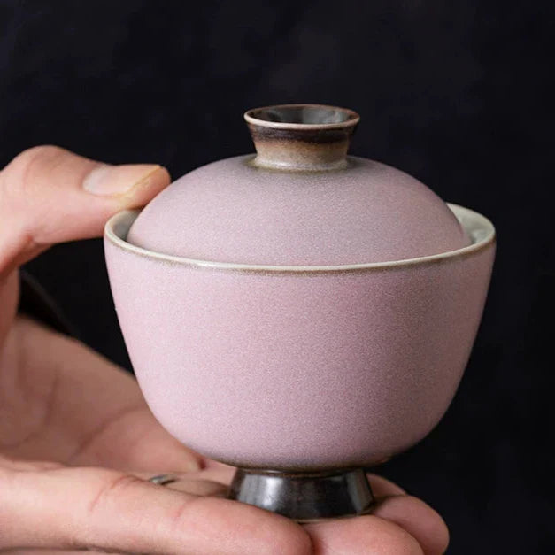 A hand holds a black pink Gaiwan
