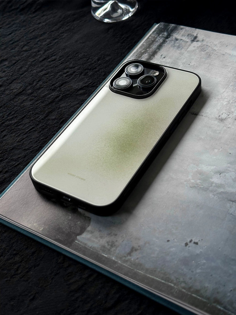 A phone case with a green and white artistic design, placed on a flat surface next to a glass with a blurred background.