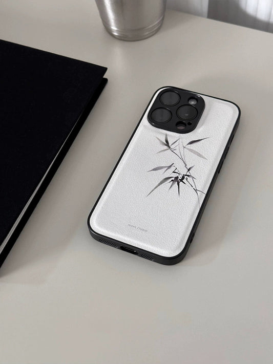 A white leather phone case with a bamboo pattern, featuring a broken bamboo design, placed on a table with a black case and a cup in the background.