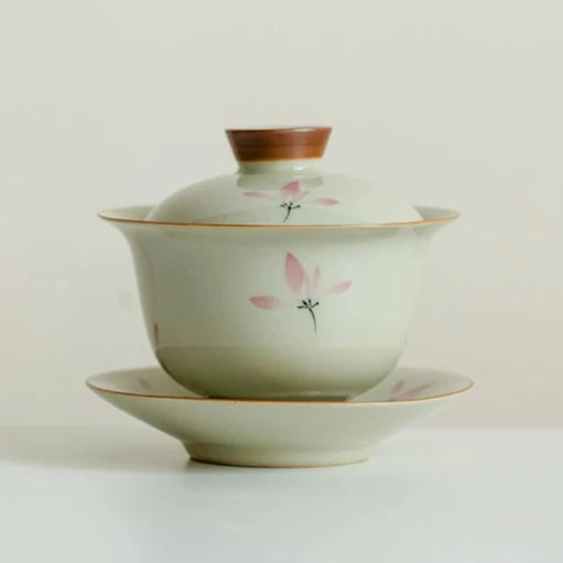 A beige and green porcelain Gaiwan with yellow flower patterns, comprising a teapot and two cups, displayed against a neutral background.