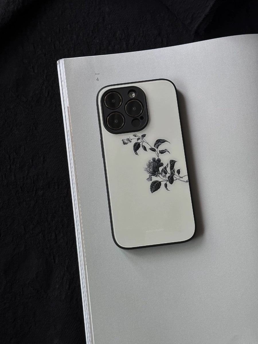 A glass phone case with a minimalist branch design, placed on a notebook with a sketch of a flower.