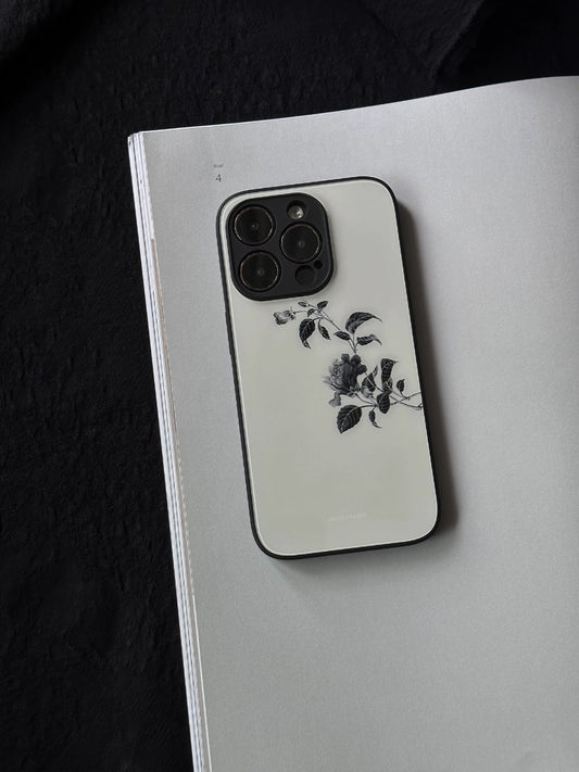 A glass phone case with a minimalist branch design, placed on a notebook with a sketch of a flower.