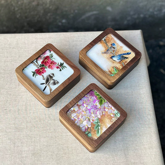 A set of three handmade black walnut wood boxes with floral and bird embroidery on the lids, displayed on a beige surface.