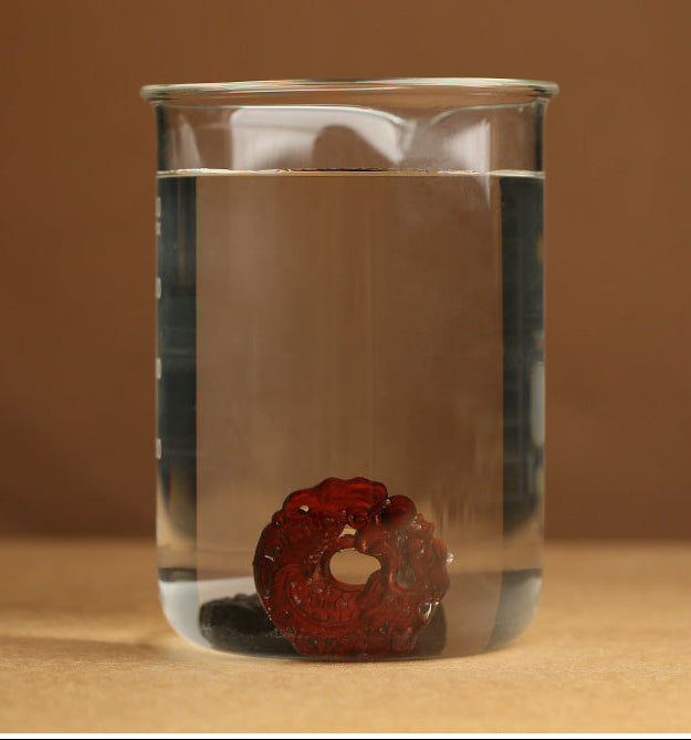 Clear glass beaker with a red object floating on water against a brown background