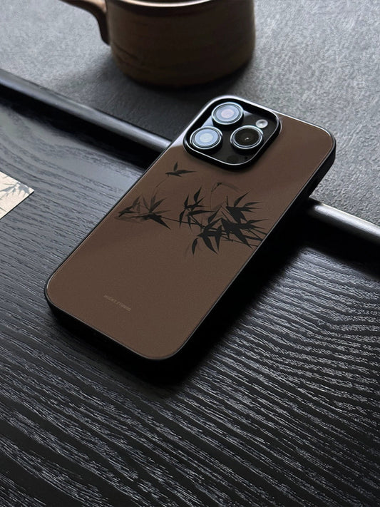 A brown phone case with a vintage bamboo design, placed on a wooden surface near a mug and a molded bamboo object, showcasing the case's pattern.